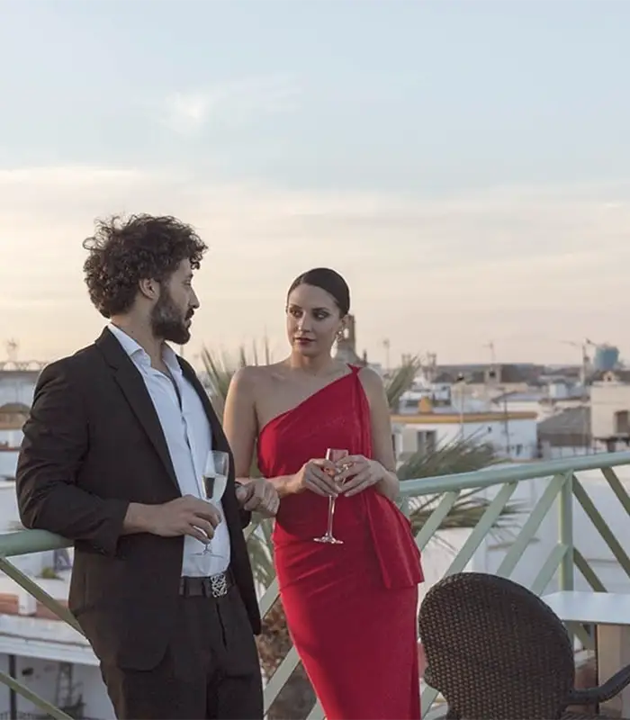 Dos personas elegantes conversan en una terraza al atardecer, con copas de vino.