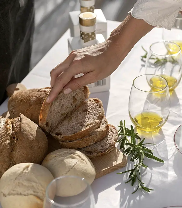 Mano tomando rebanada de pan en mesa con aceite y ramitas de romero.