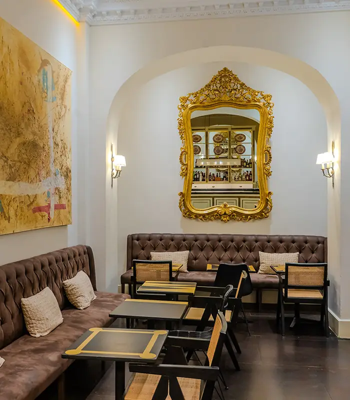 Elegante cafeter&iacute;a con espejos dorados y sof&aacute;s marrones almohadillados.