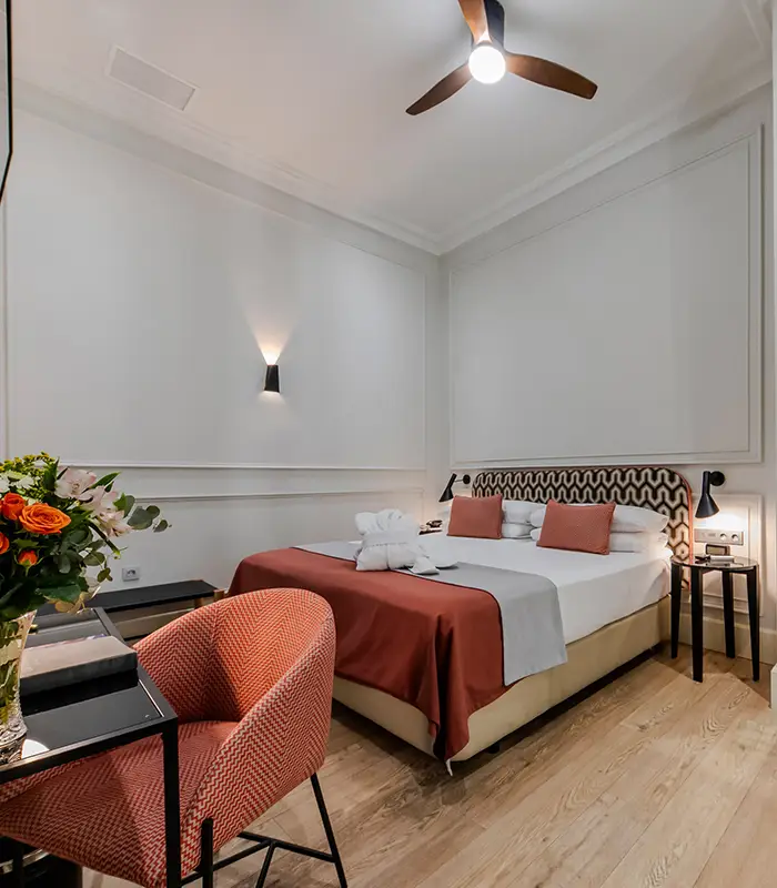 Habitaci&oacute;n moderna con cama doble, flores y sill&oacute;n rojo.