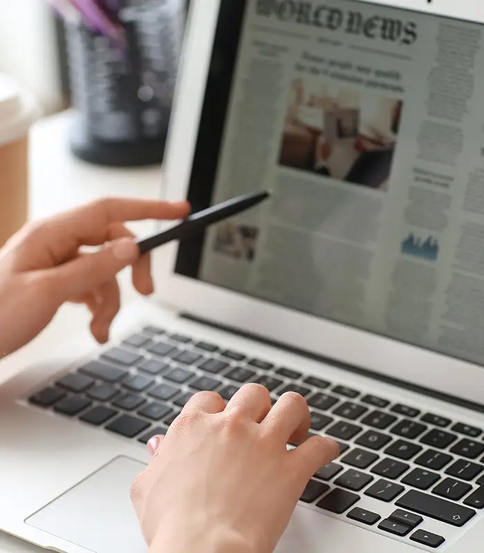 Manos usando una laptop mientras revisan un art&iacute;culo de noticias.