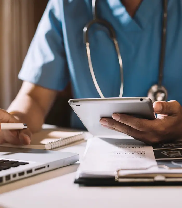 M&eacute;dico con bata azul usando una tablet en un escritorio.
