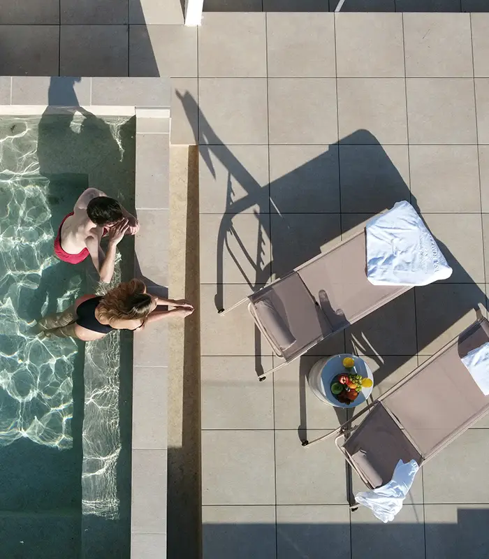 Vista a&eacute;rea de una piscina con dos personas y tumbonas cercanas.