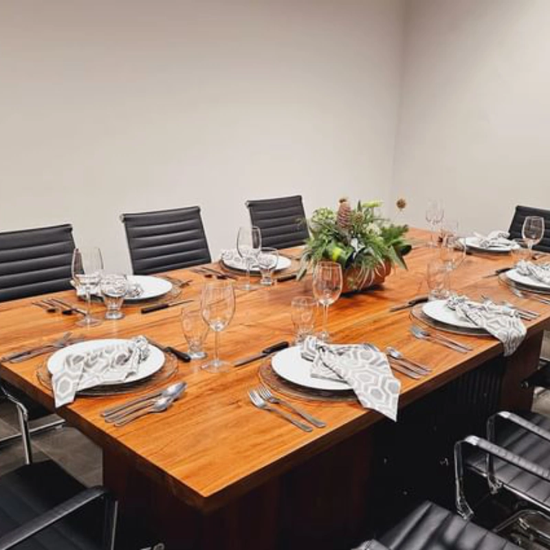 Mesa de madera para ocho personas, elegantemente preparada con platos, copas y centro de flores.