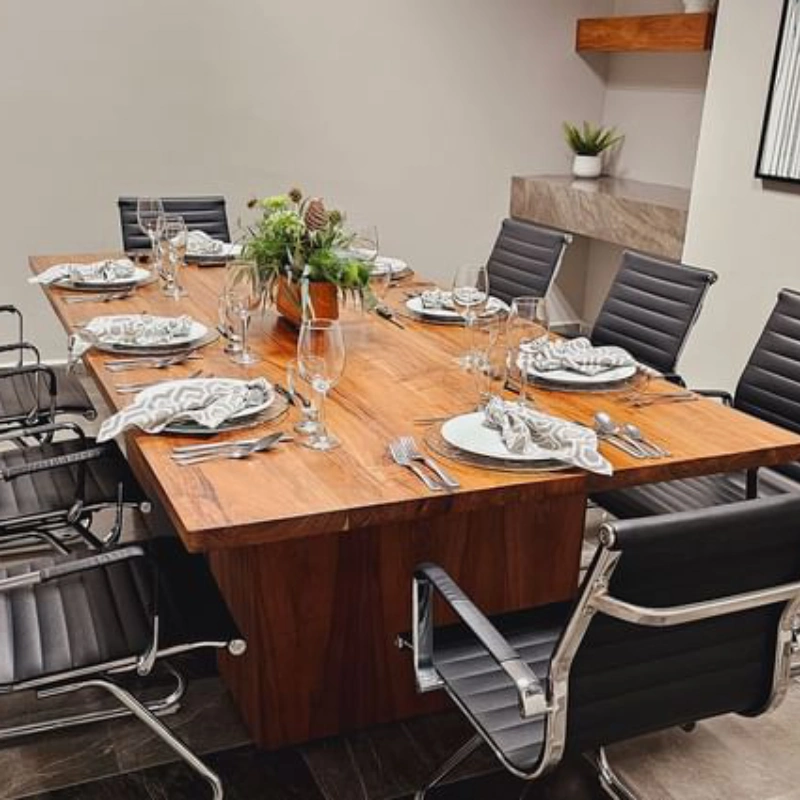 Mesa de madera para ocho personas con sillas negras, vajilla blanca y centro de mesa con plantas.