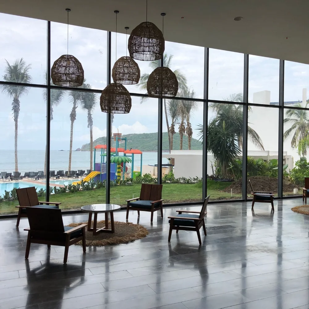 Sala con vista al mar, sillas de madera y l&aacute;mparas de mimbre colgantes.