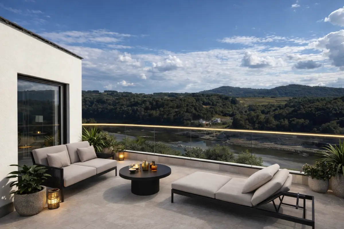 Terraza moderna con sofás y vistas a un valle y río, cielo nublado.