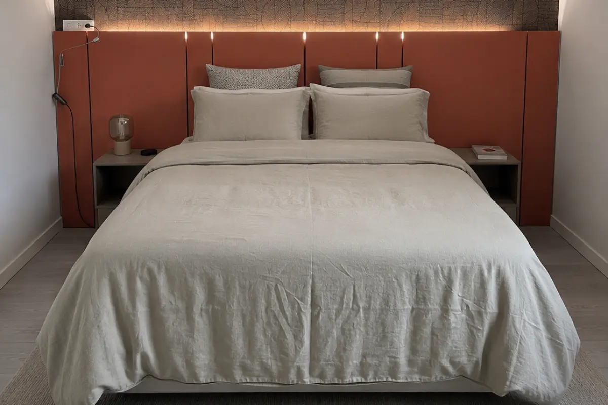 Cama con sábanas blancas, almohadas y cabecero de color cobrizo, luces LED