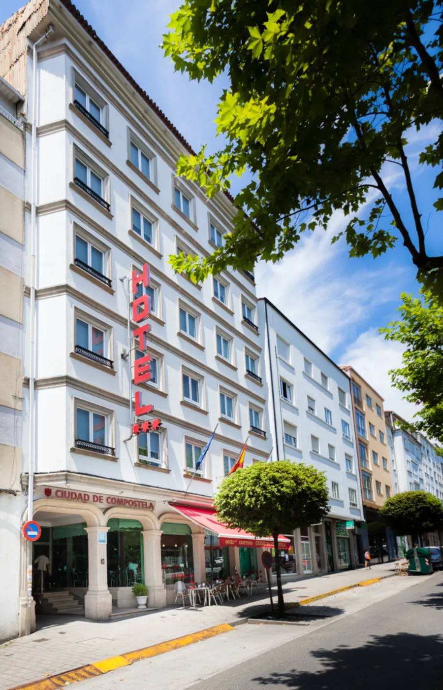Fachada de hotel urbano con letrero y árboles bajo un cielo azul.