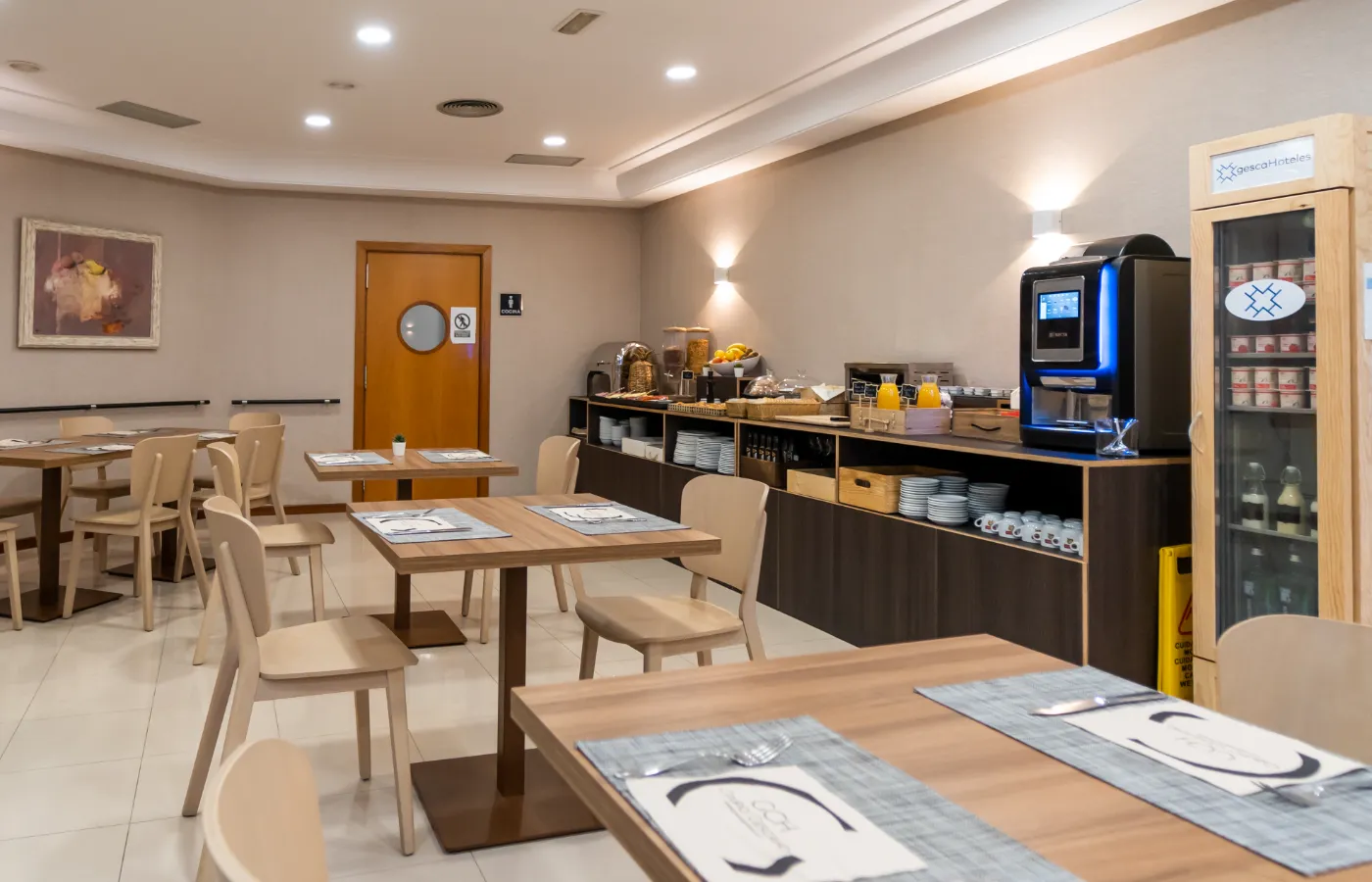 Comedor moderno con mesas y buffet de desayuno, muebles de madera clara.