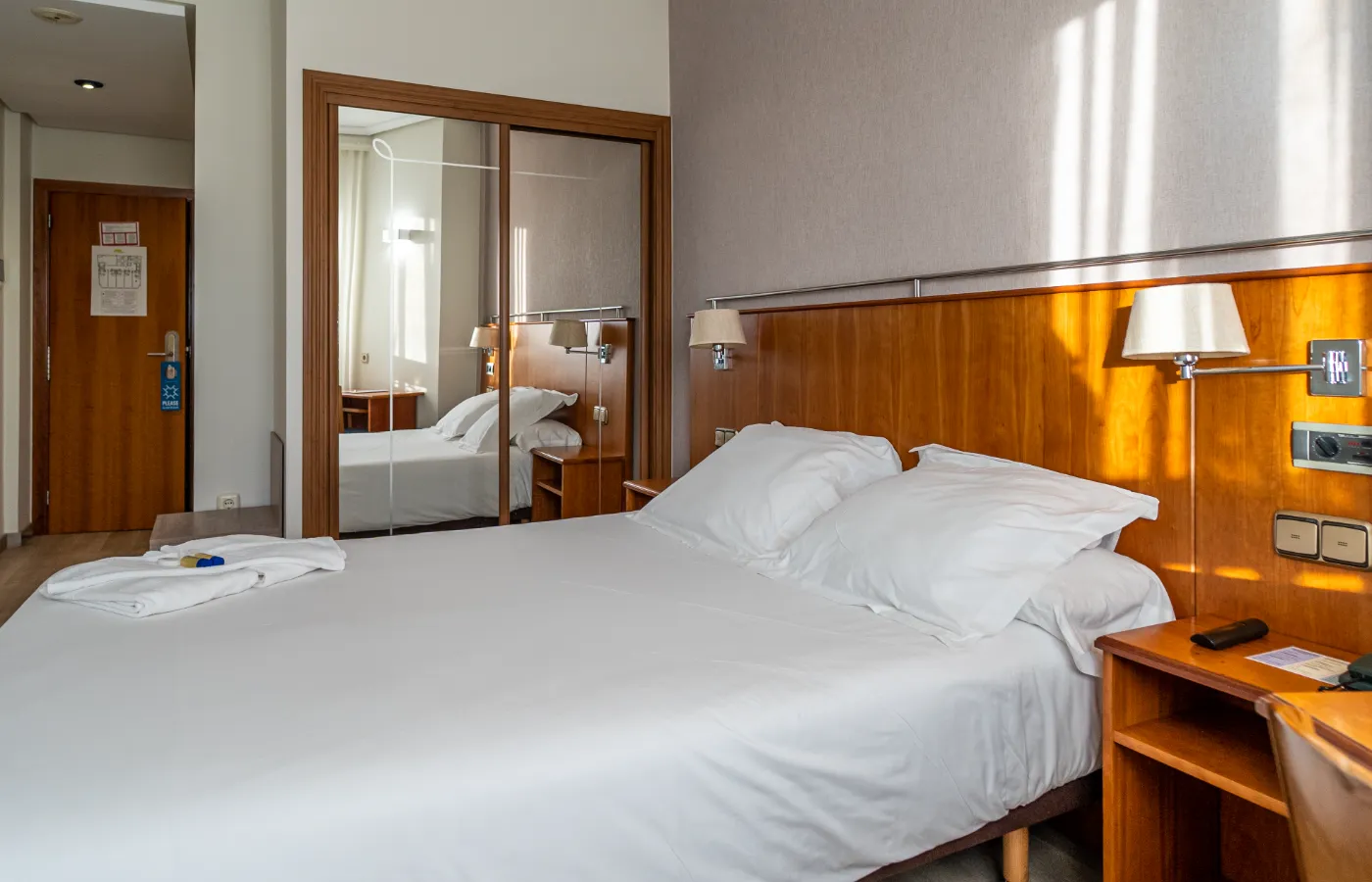 Habitación de hotel con cama doble, espejo y muebles de madera.