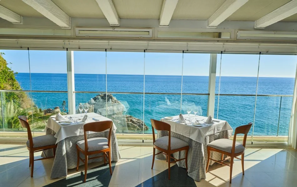 Restaurante con vista al mar, mesas y sillas listas para comensales.
