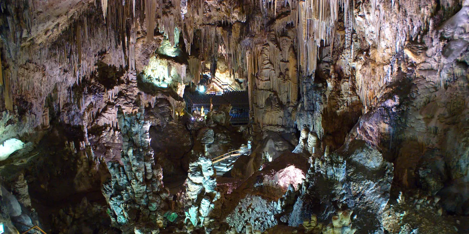 Interior de una cueva con estalactitas y un camino iluminado.