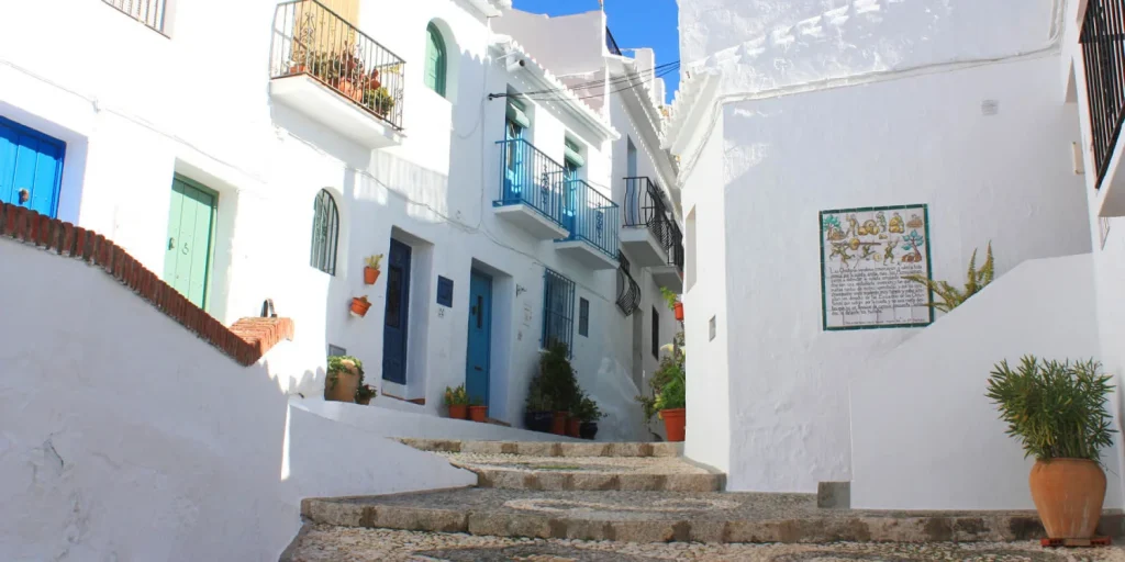 Callej&oacute;n empedrado con casas blancas y puertas azules en un pueblo mediterr&aacute;neo.