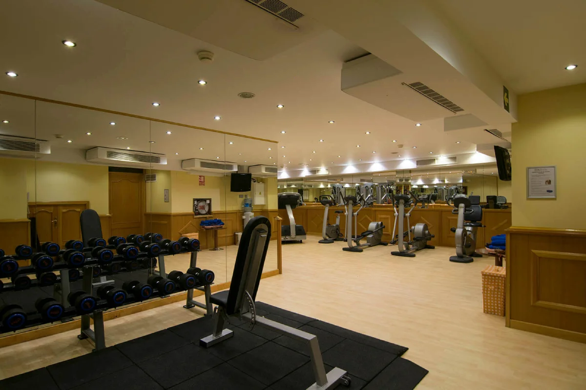 Gimnasio vac&iacute;o con pesas y m&aacute;quinas de ejercicio en una sala con espejos.