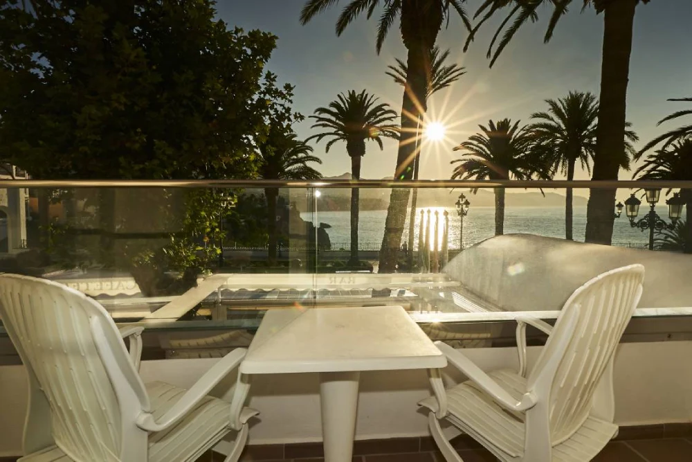 Terraza con vista al mar, al atardecer, con sillas y mesa blanca.