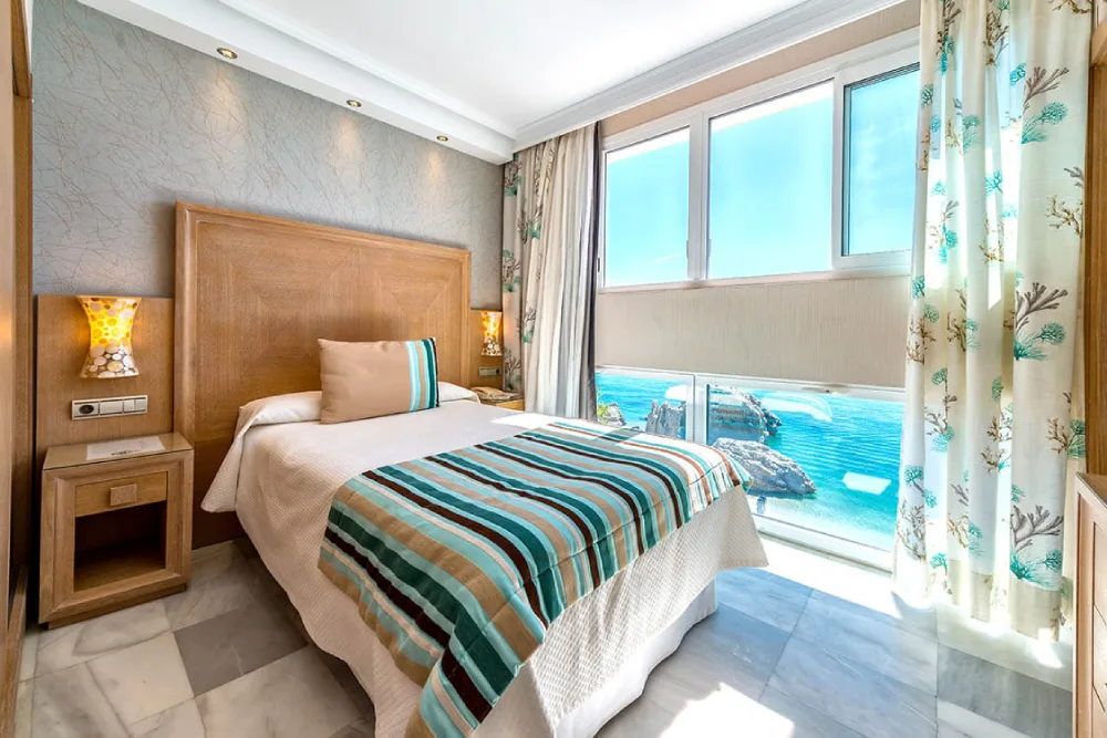 Habitaci&oacute;n luminosa con cama individual y vista al mar desde la ventana.