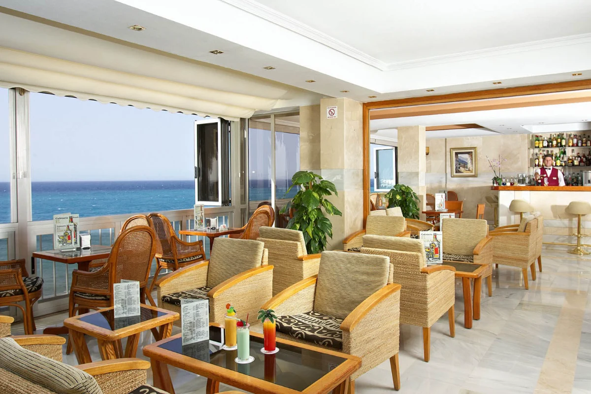 Sala de estar moderna con vista al mar, barra y muebles de mimbre.
