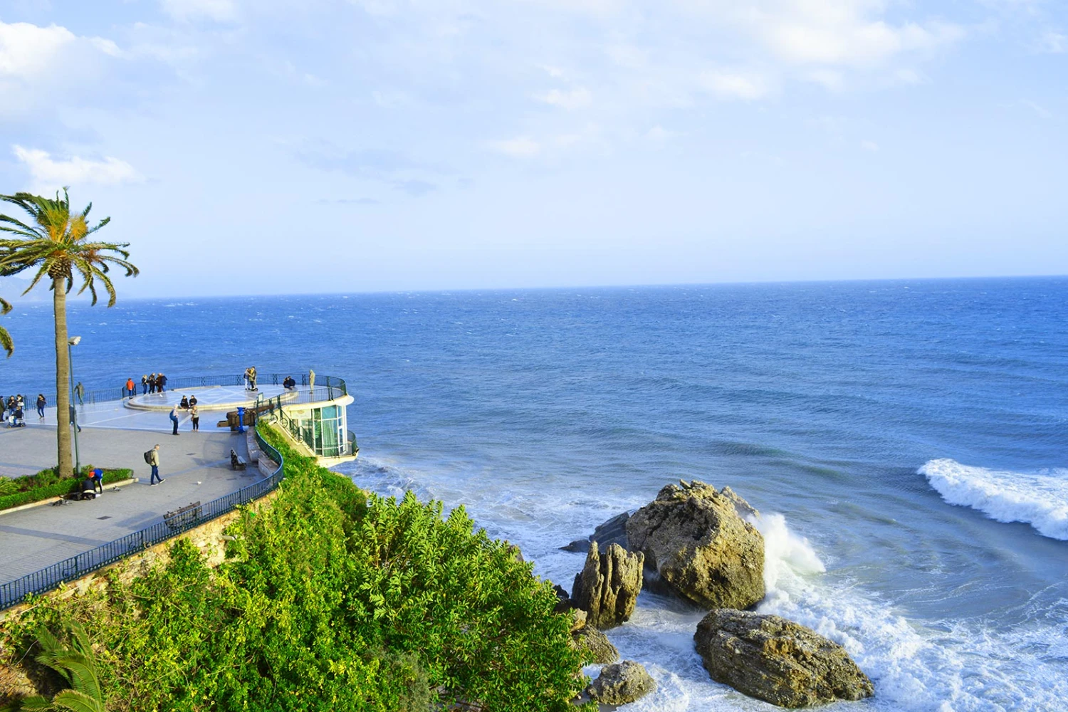 Mirador con palmera junto a un acantilado con vista al mar y rocas.