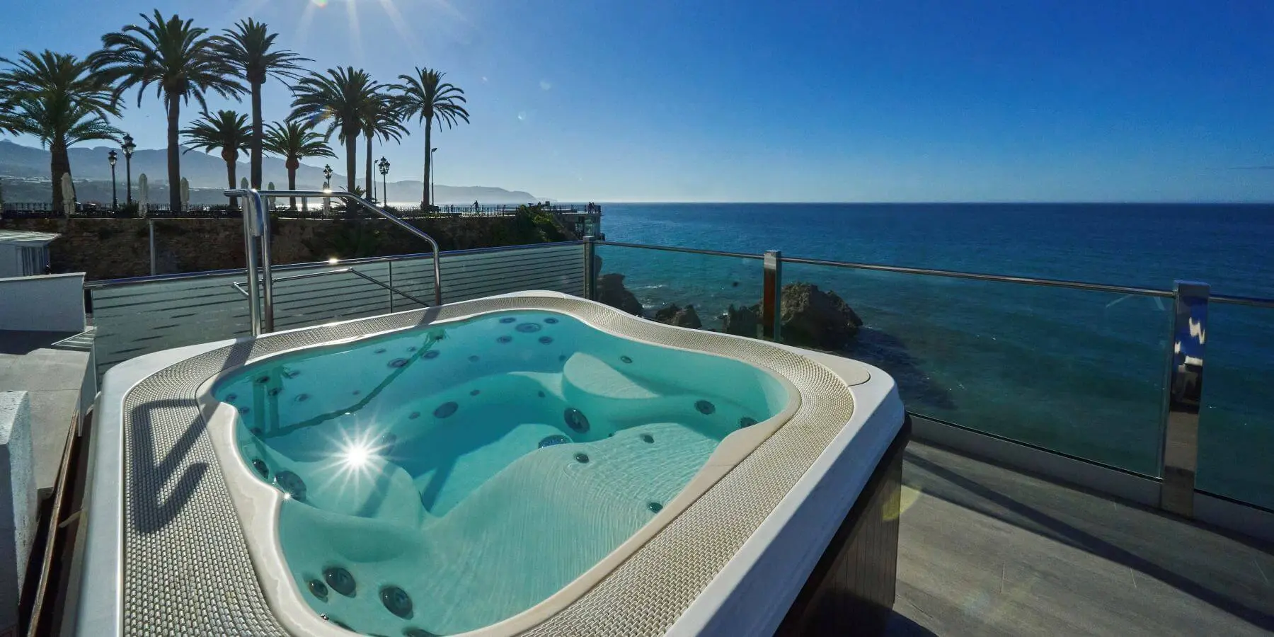 Jacuzzi con vista al mar y palmeras bajo un cielo azul y soleado.