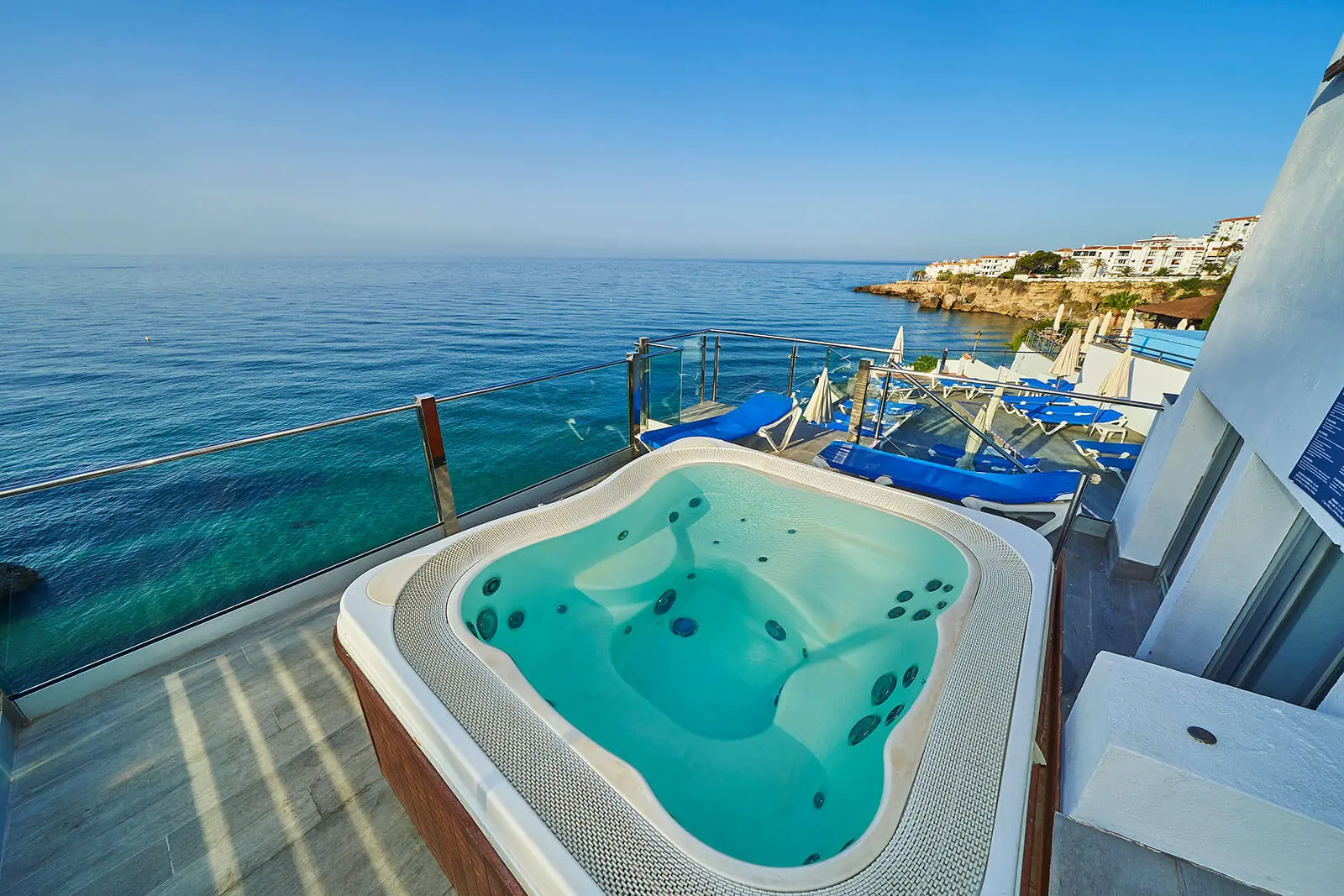 Jacuzzi con vista al mar y tumbonas azules bajo un cielo despejado.