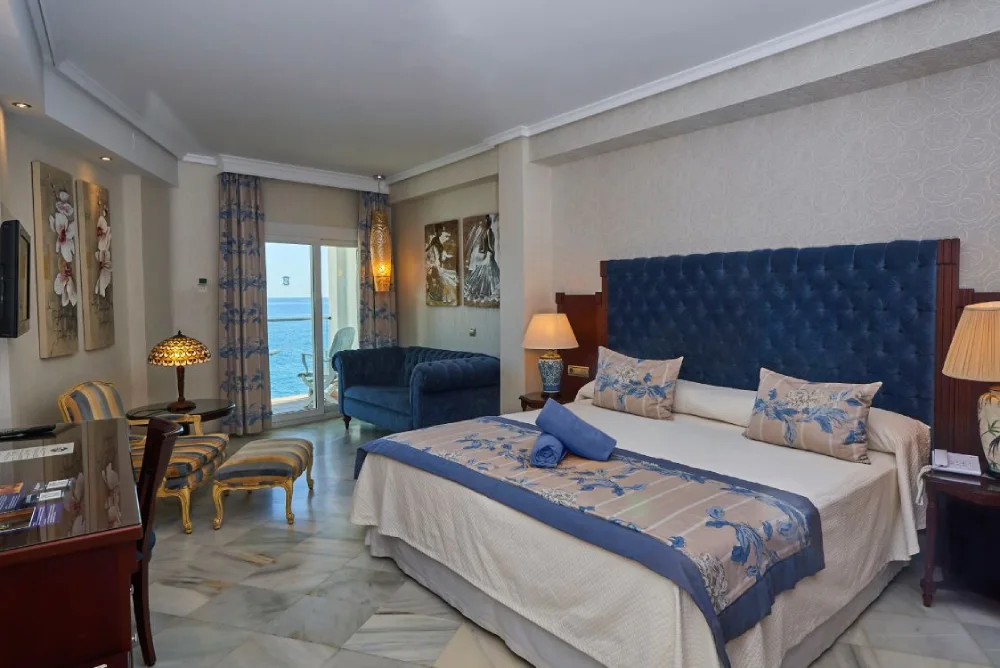 Habitaci&oacute;n elegante con cama doble, vista al mar y decoraci&oacute;n en tonos azules.