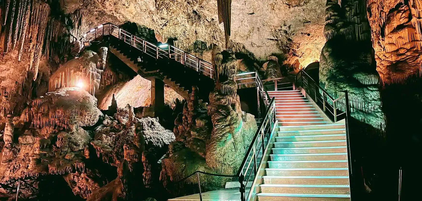 Escaleras iluminadas en una cueva con estalactitas y estalagmitas.