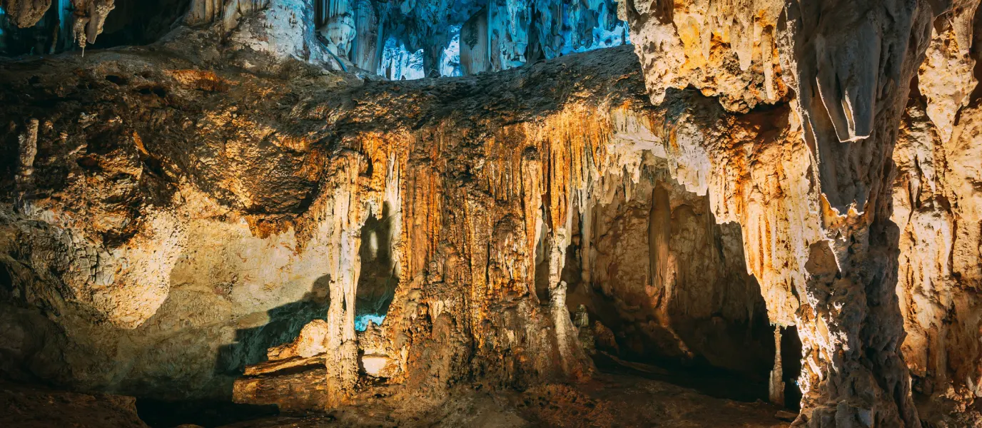 Cueva con estalactitas y estalagmitas iluminadas en tonos c&aacute;lidos y fr&iacute;os.