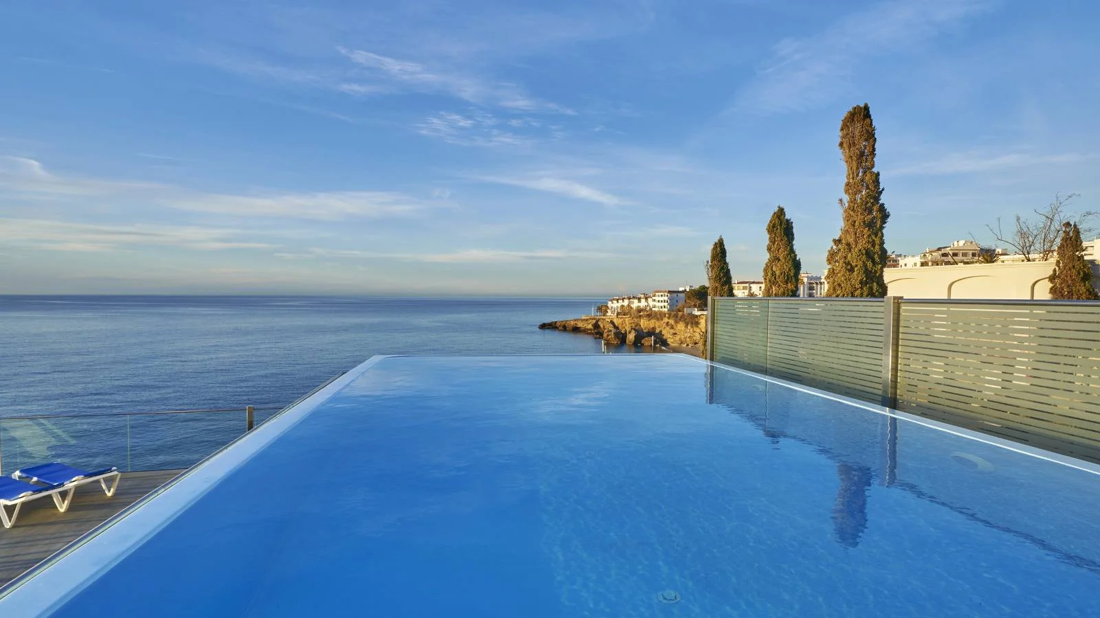 Piscina infinita con vista al mar y acantilado bajo un cielo despejado.