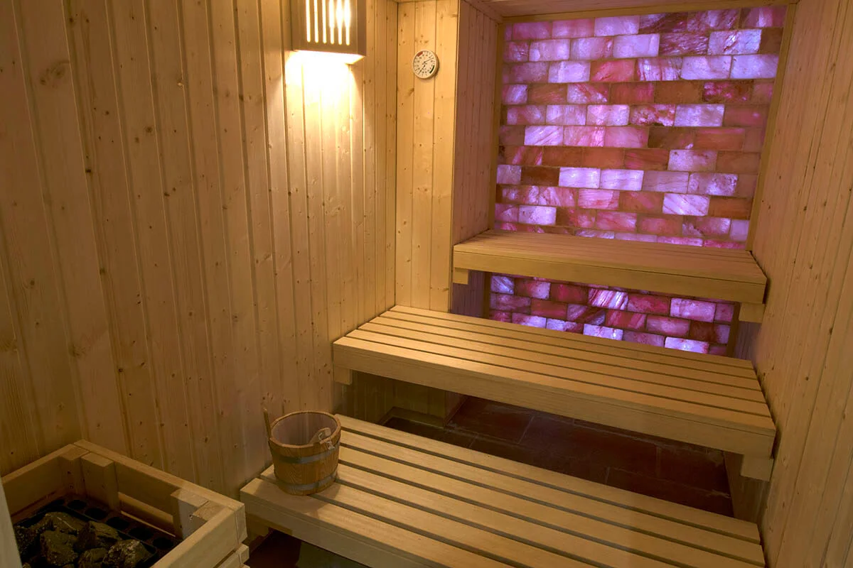 Sauna de madera con pared iluminada de ladrillos rosados y un cubo al frente.