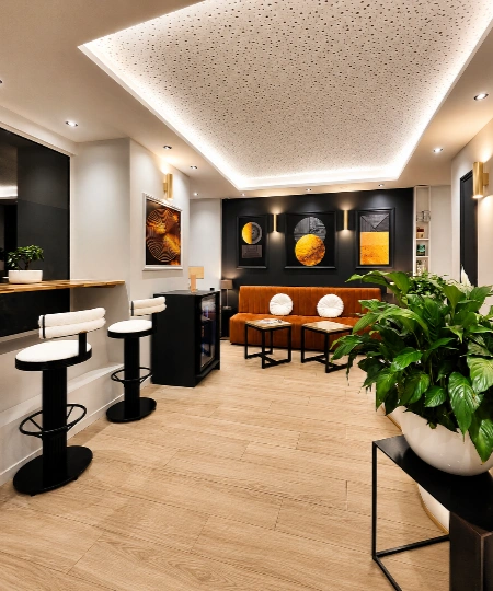 Salon moderne avec comptoir, tabourets et plantes, &eacute;clairage au plafond.