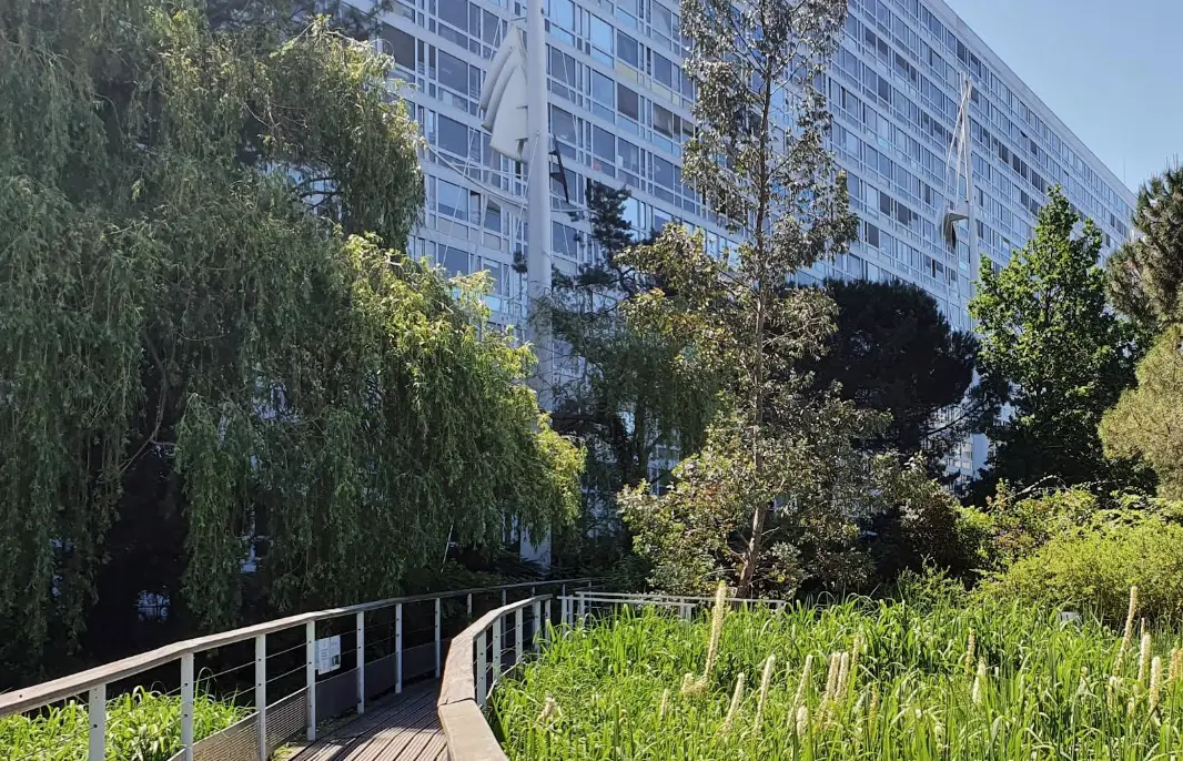 Fa&ccedil;ade d&rsquo;un immeuble moderne avec arbres et jardin le long d&rsquo;une passerelle