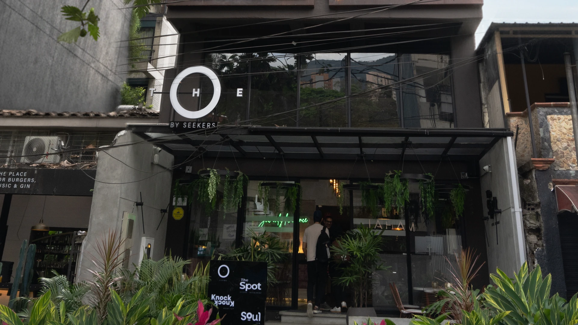 Fachada de un caf&eacute; moderno con plantas y letrero circular.