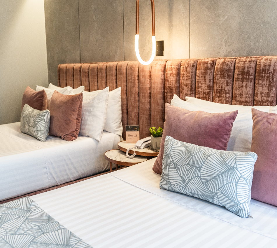 Habitaci&oacute;n con dos camas, cojines decorativos y una l&aacute;mpara moderna.