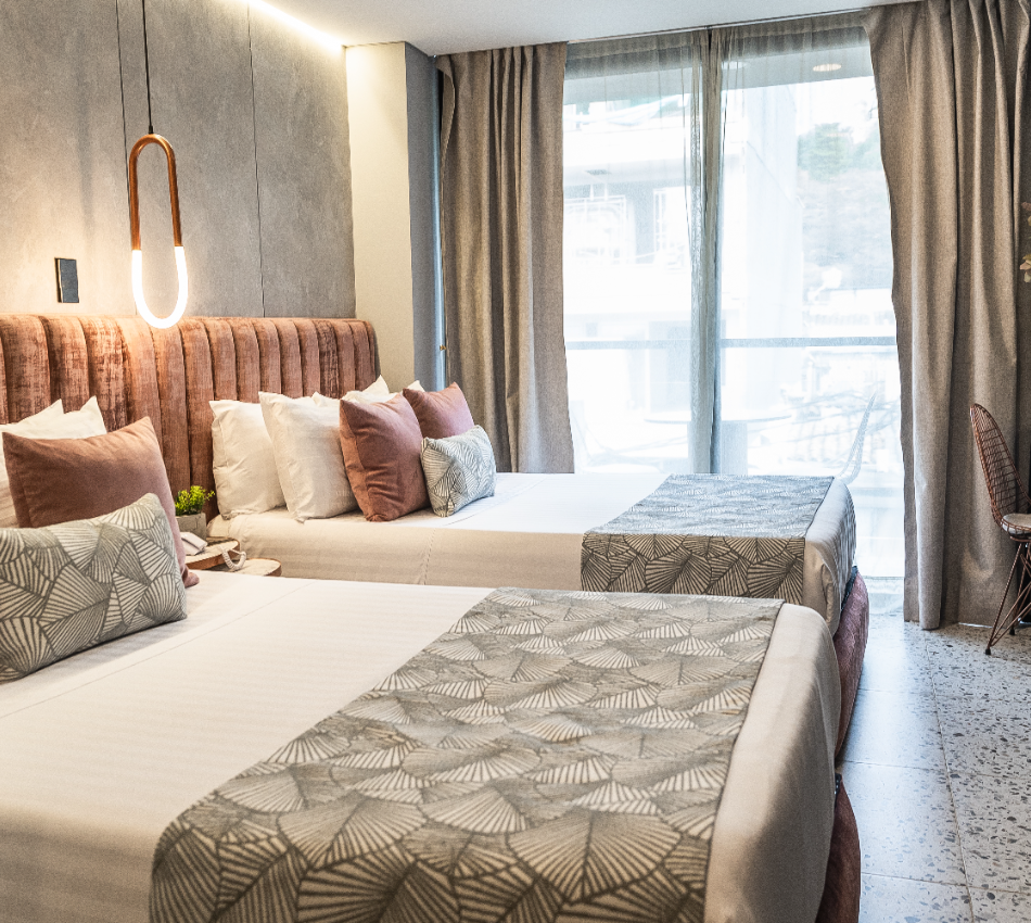 Habitaci&oacute;n de hotel moderna con dos camas y ventana amplia con cortinas.