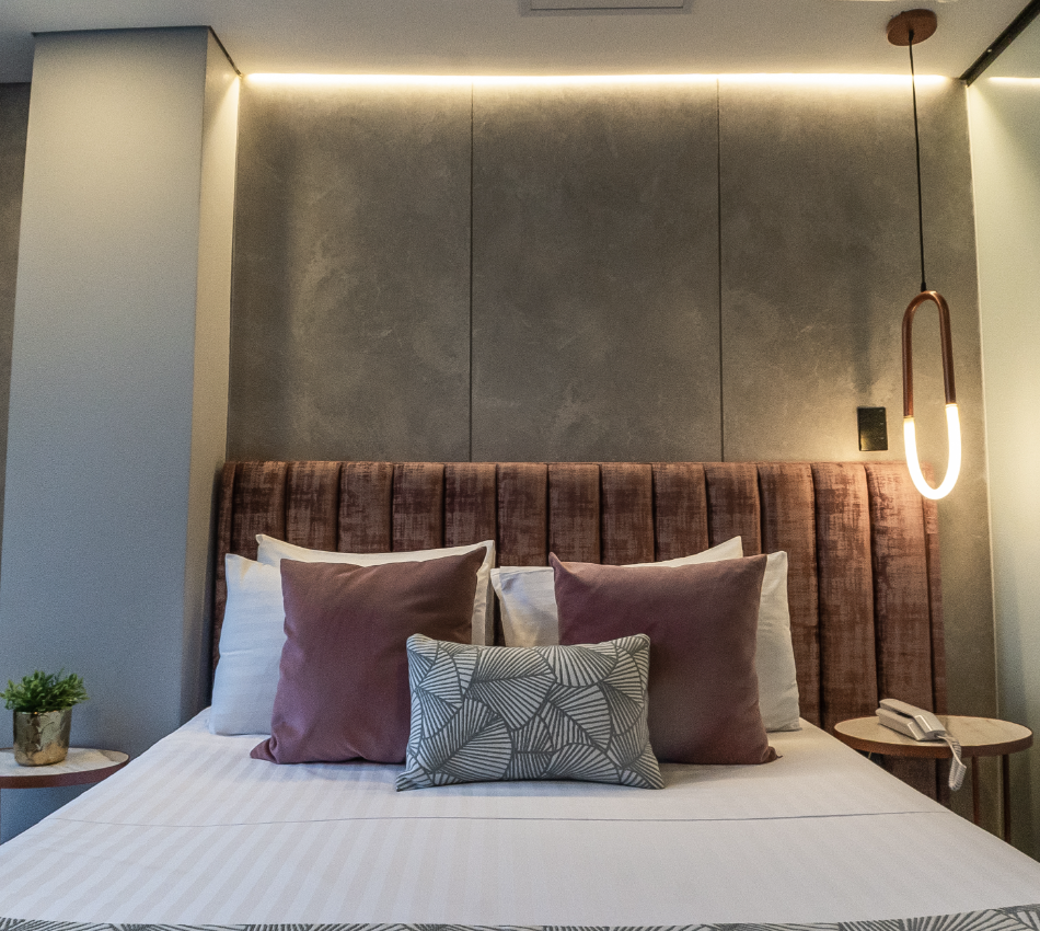 Cama moderna con cojines y l&aacute;mpara colgante en habitaci&oacute;n elegante.