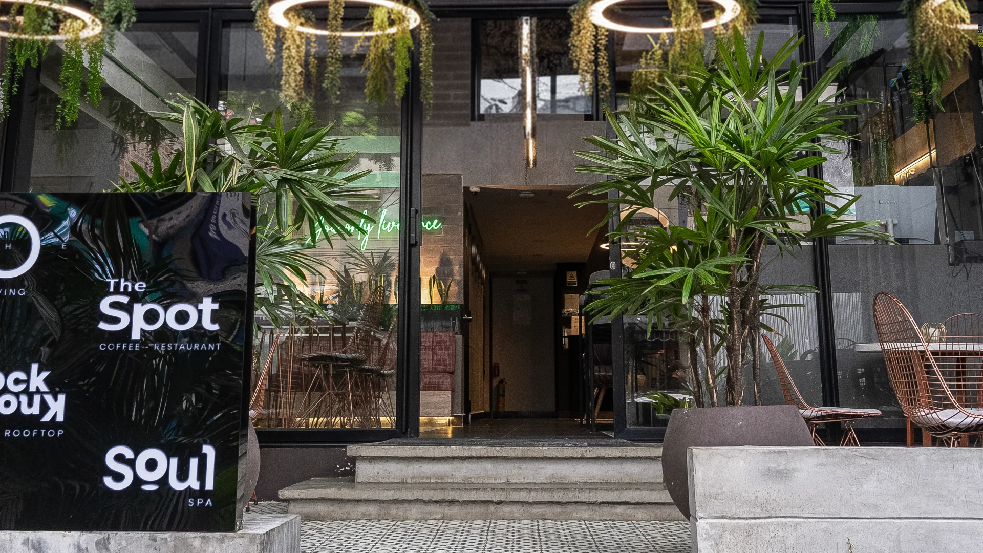 Entrada de cafeter&iacute;a moderna con plantas y letrero luminoso.