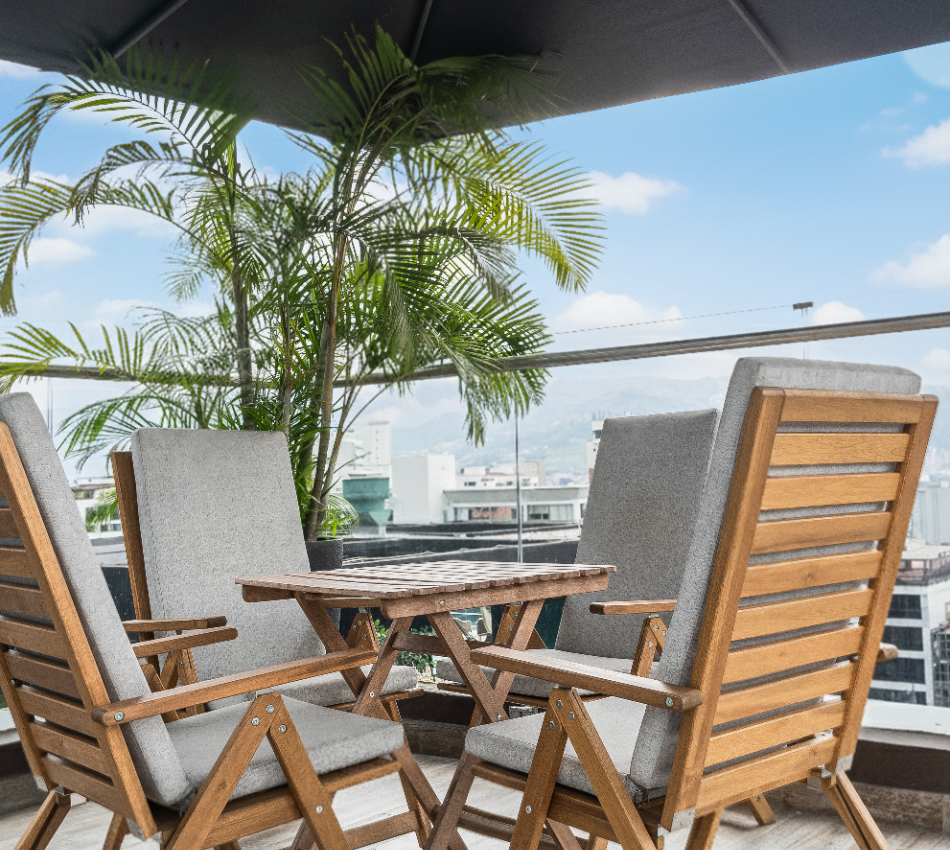 Terraza con sillas de madera y plantas bajo un cielo azul.