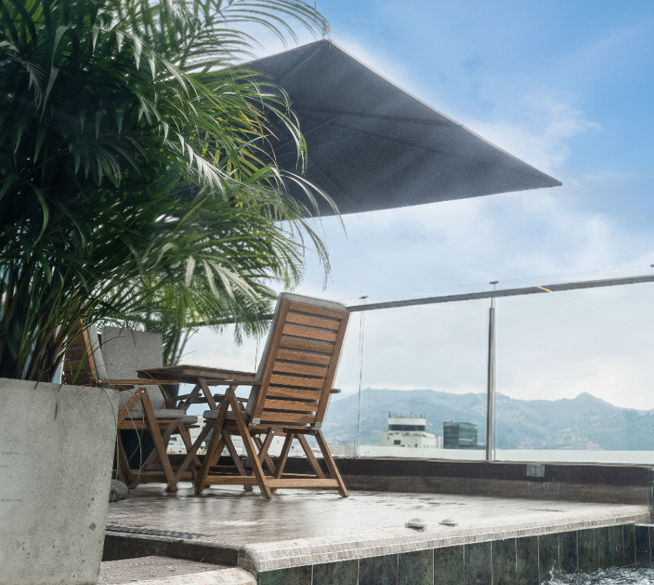 Terraza con sillas de madera, plantas y una sombrilla bajo el cielo azul.