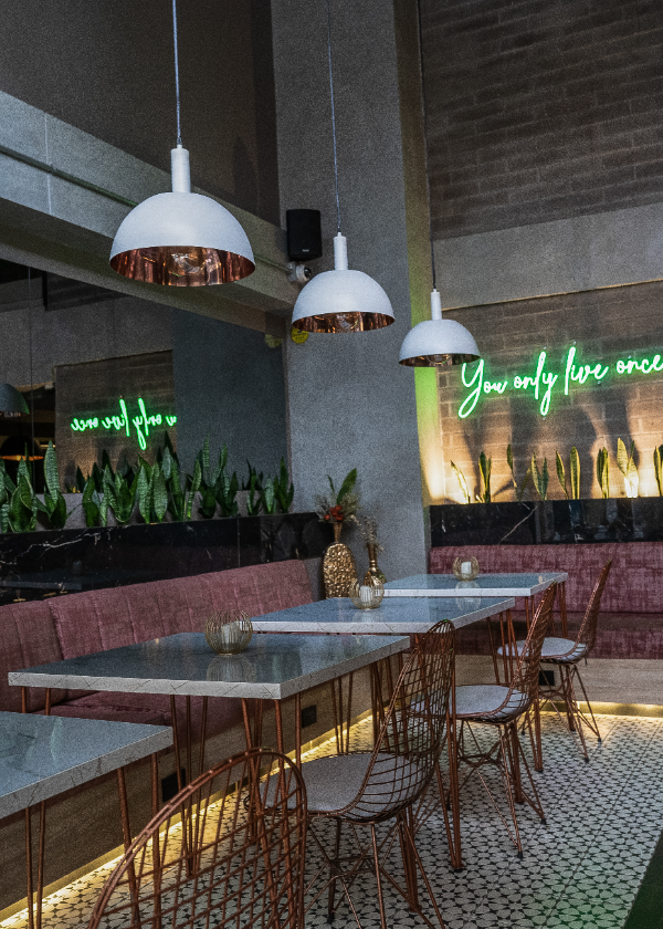 Restaurante moderno con mesas de m&aacute;rmol y luces de ne&oacute;n verde en la pared.