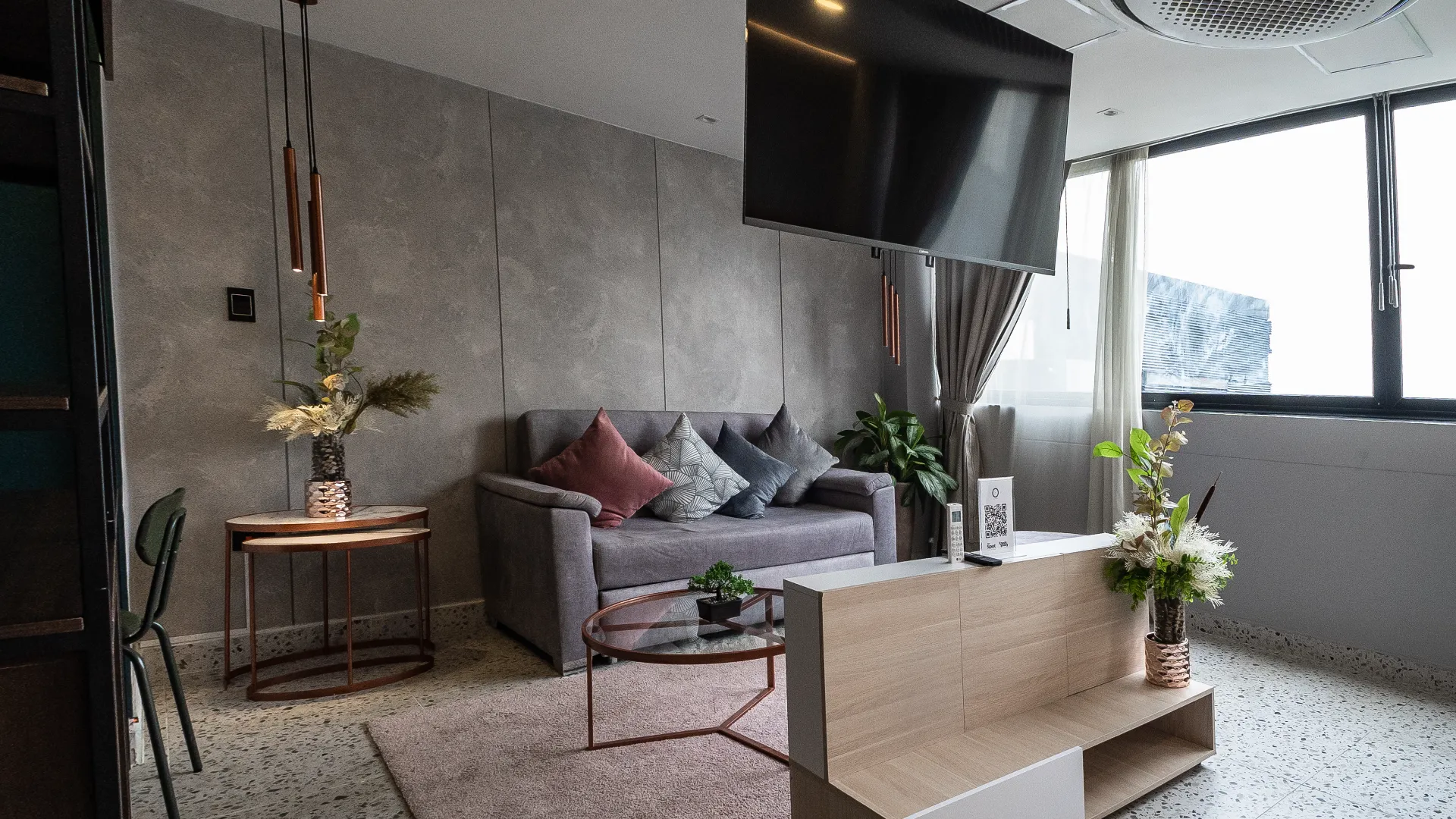 Sala moderna con sof&aacute;, cojines, mesa de vidrio y plantas decorativas.