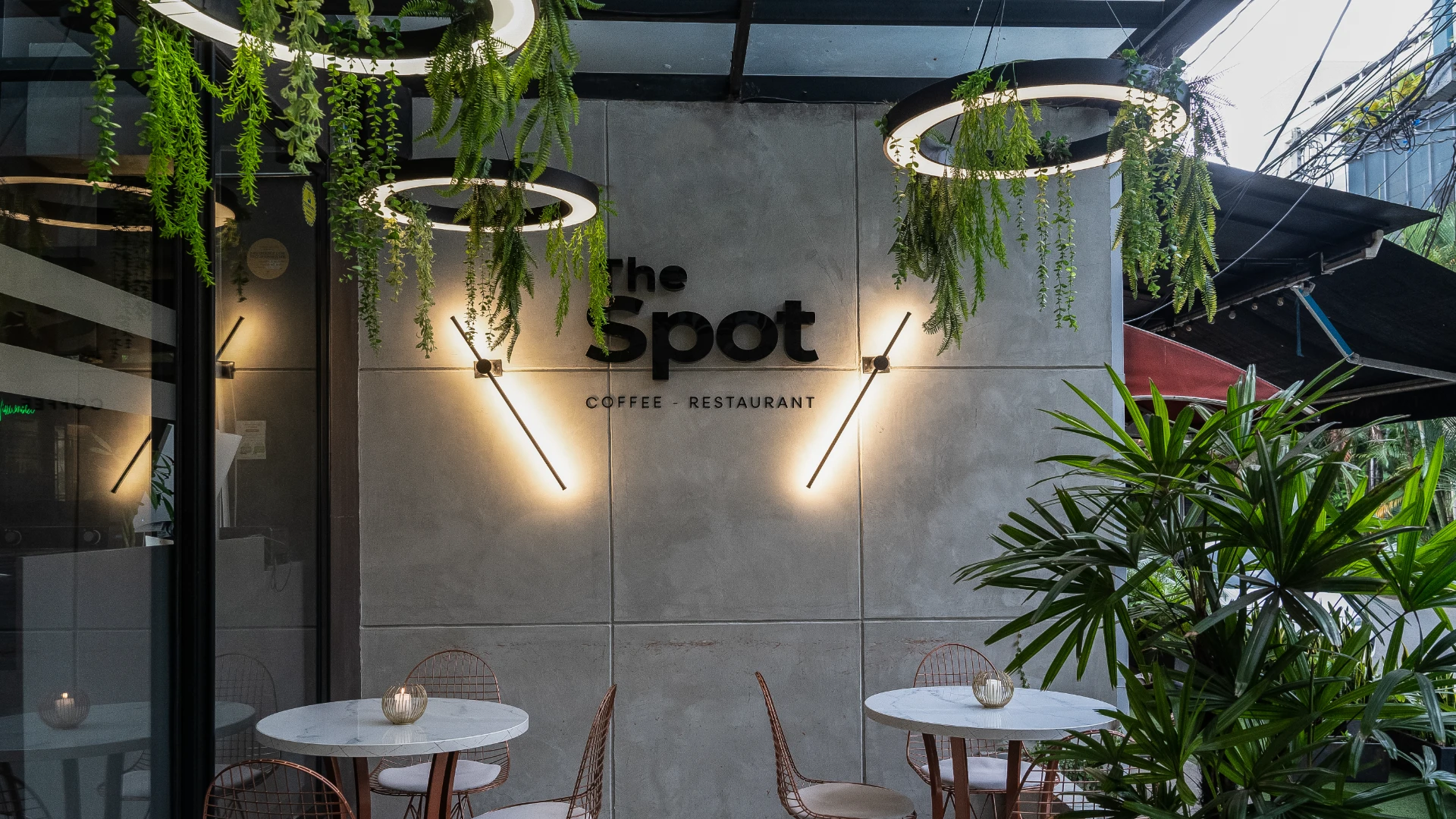 Caf&eacute; con mesas al aire libre y decoraci&oacute;n de plantas colgantes.
