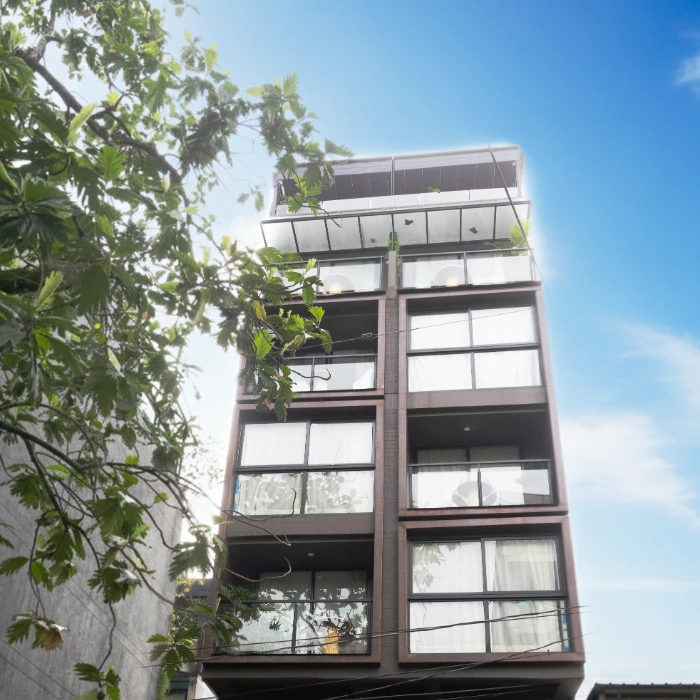 Edificio moderno de cinco pisos con cielo azul y ramas de &aacute;rbol.