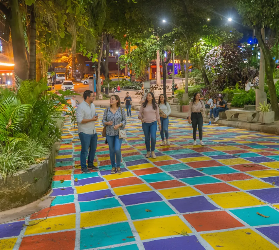 Gente caminando por una calle colorida en una ciudad por la noche.