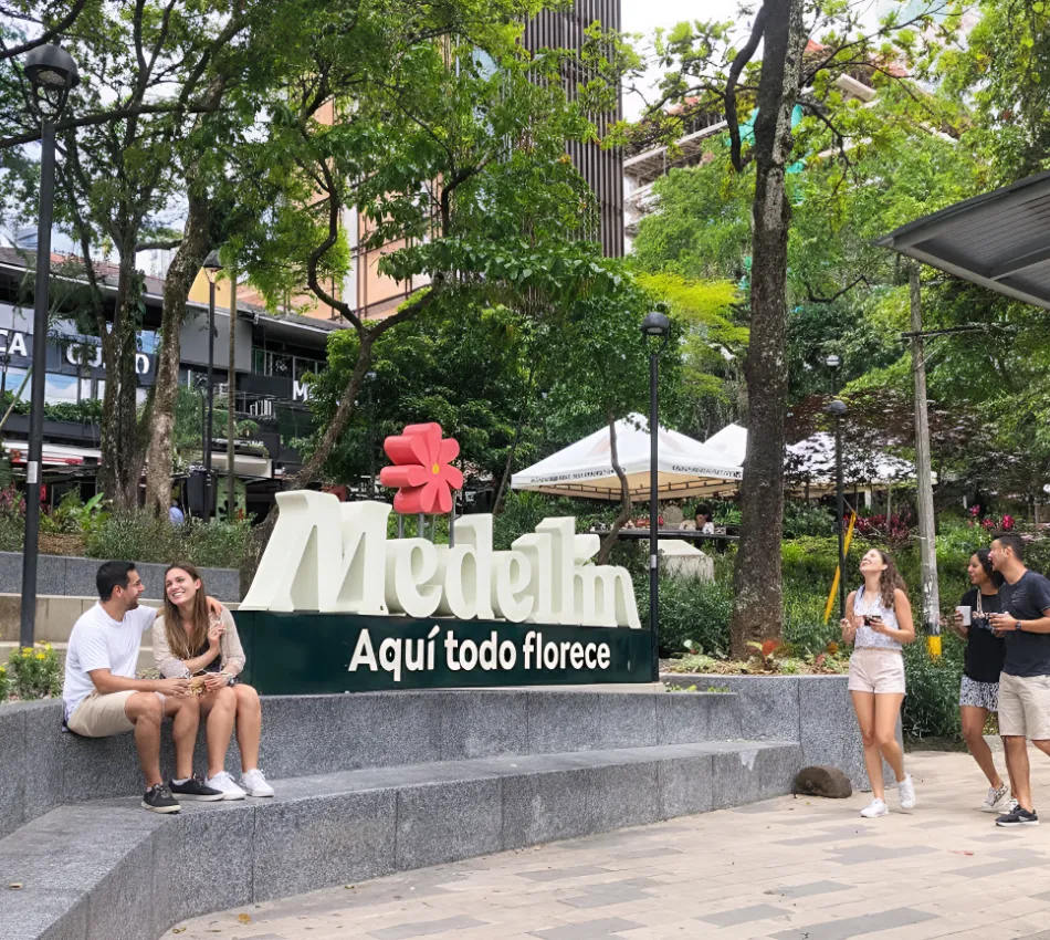 Gente junto al letrero "Medell&iacute;n: Aqu&iacute; todo florece" en un parque urbano.