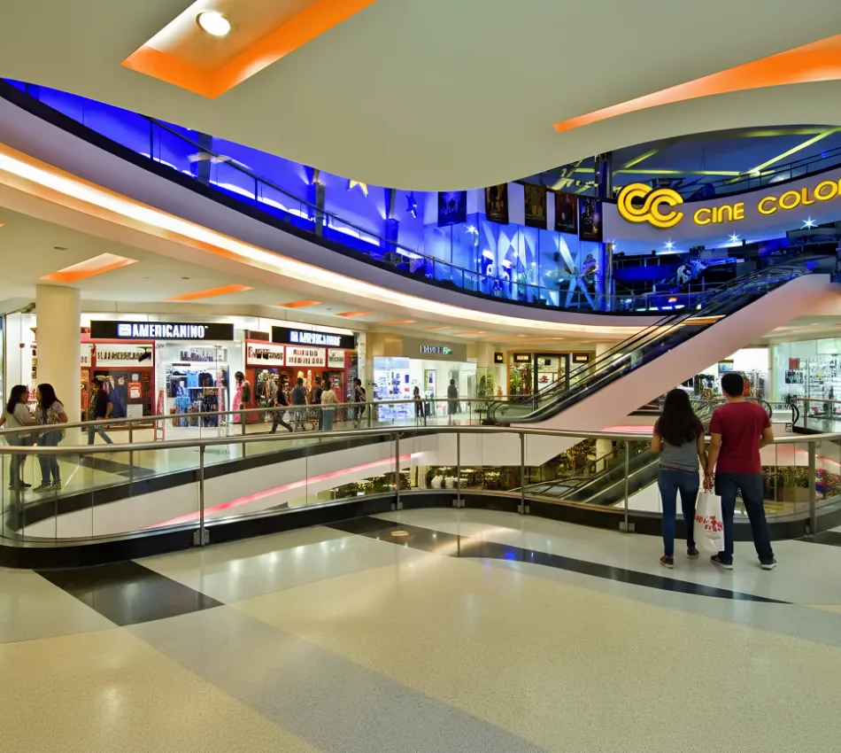 Centro comercial con tiendas y cine, gente caminando y escaleras el&eacute;ctricas.