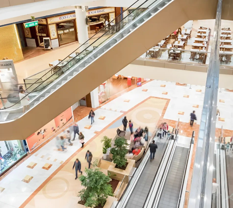 Centro comercial con escaleras mec&aacute;nicas y personas caminando.