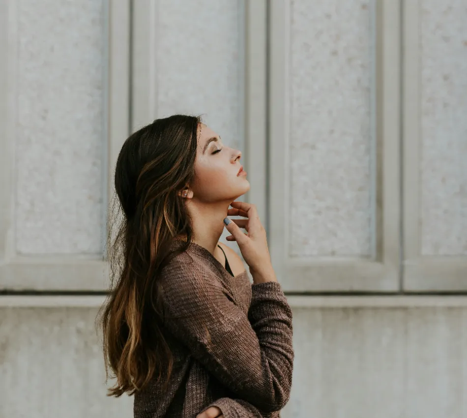 Mujer de perfil en su&eacute;ter marr&oacute;n, posa frente a una pared clara.