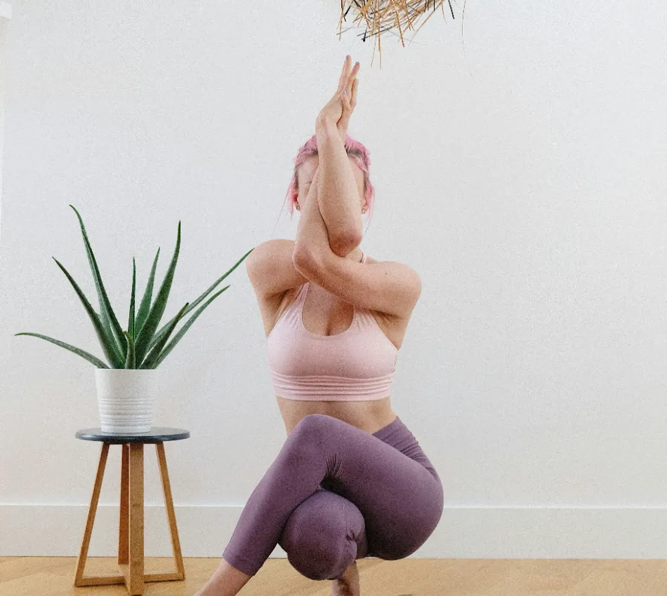 Persona haciendo yoga junto a una planta en maceta, fondo blanco.