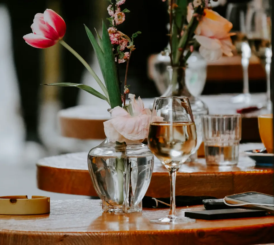Mesa con copa de vino, flores y objetos diversos.